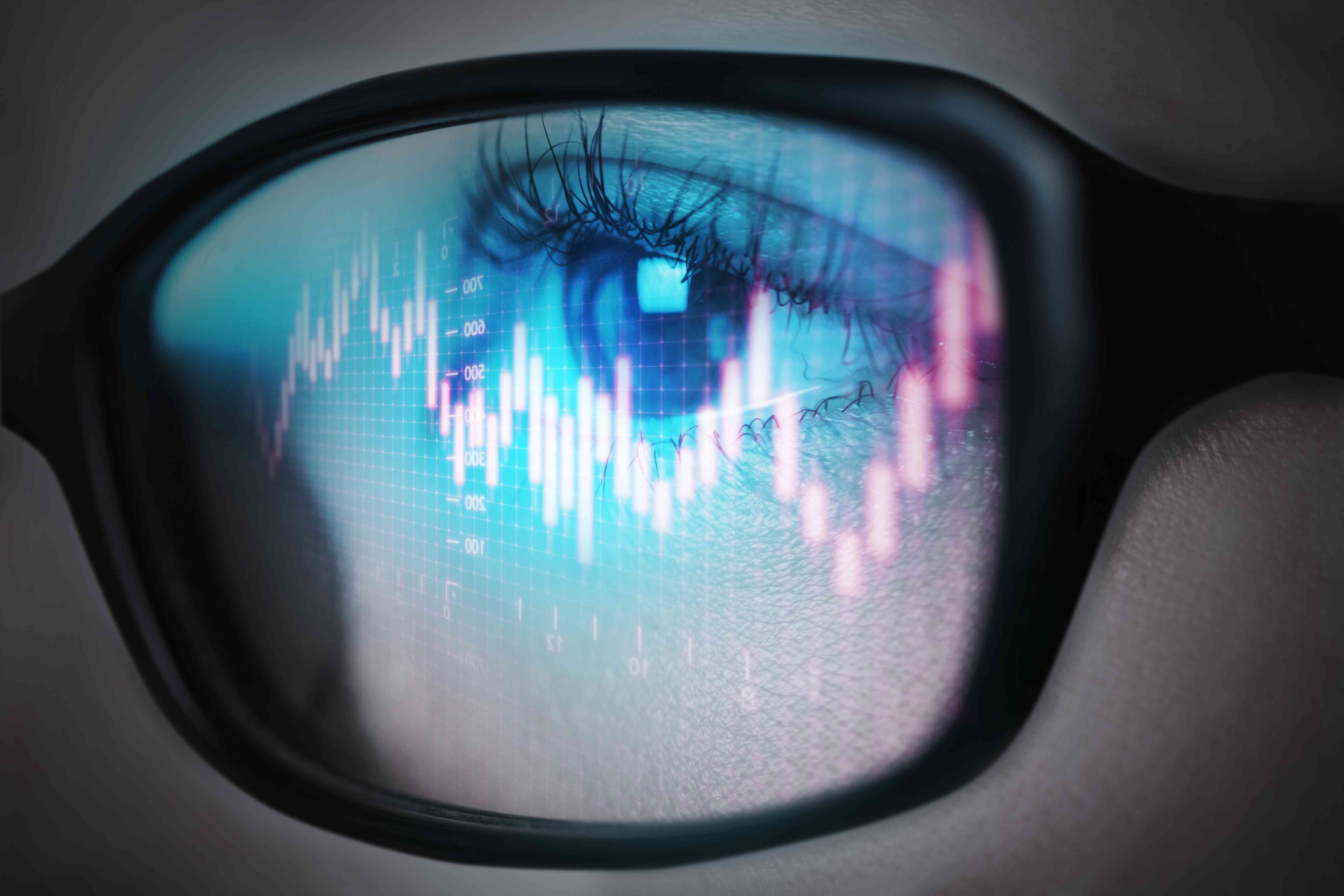 A person looking through eyeglasses with charts reflected on the lense.